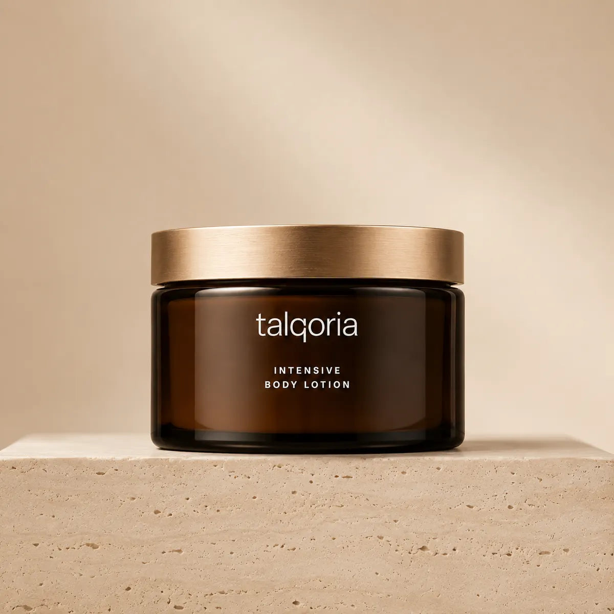 A dark amber glass jar of talqoria Intensive Body Lotion with a brushed gold lid, displayed on a textured beige stone pedestal against a matching beige background.