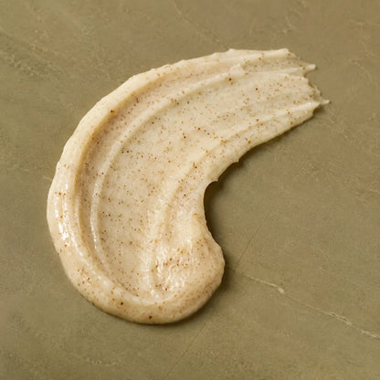 A thick, creamy beige cosmetic or skincare cream swatch with fine brown specks, swirled on a textured olive-green surface.