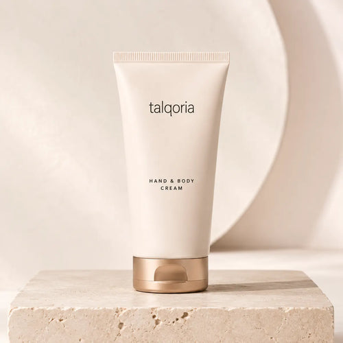 A tube of talqoria Hand & Body Cream standing upright on a textured stone slab, with a soft beige background and a large circular decorative element behind it.