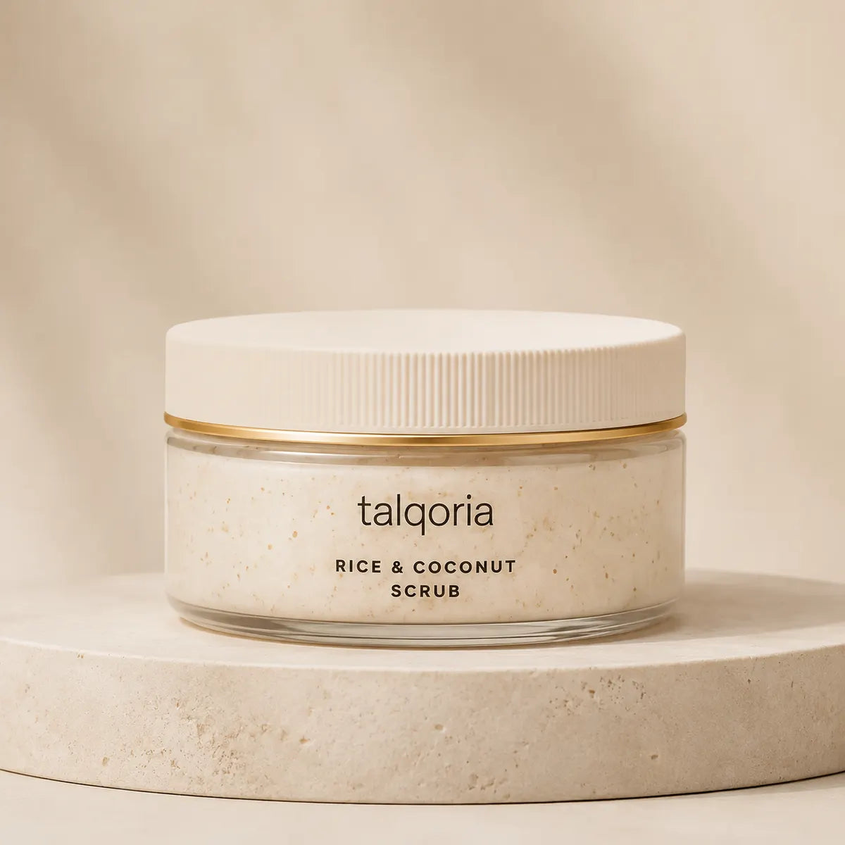 A jar of talqoria Rice & Coconut Scrub with a white lid and gold band, sitting on a round beige stone pedestal against a warm beige background.