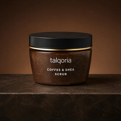 A jar of talqoria Coffee & Shea Scrub, featuring a dark brown textured body with a black lid and a thin gold accent band, set on a dark stone surface against a warm brown background.
