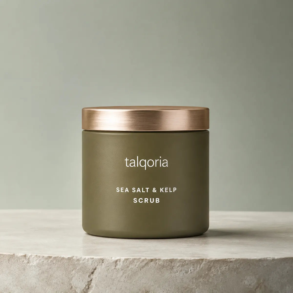 A matte olive green jar of talqoria Sea Salt & Kelp Scrub with a brushed rose gold lid, sitting on a light stone surface against a muted sage green background.
