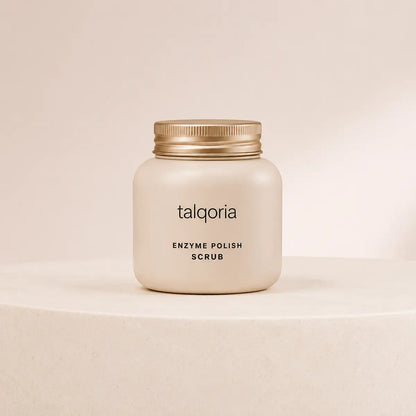 A frosted cream-colored jar of talqoria Enzyme Polish Scrub with a metallic gold screw cap, displayed on a matching cream-colored pedestal against a neutral beige background.