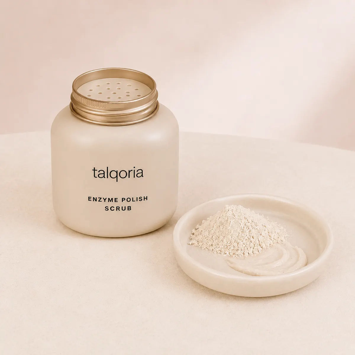 A frosted cream-colored jar of talqoria Enzyme Polish Scrub with a gold lid, shown next to a small dish containing the white scrub powder.