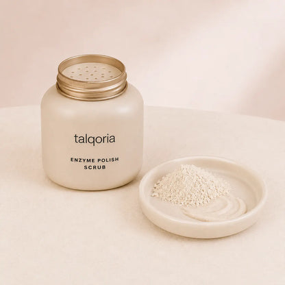 A frosted cream-colored jar of talqoria Enzyme Polish Scrub with a gold lid, shown next to a small dish containing the white scrub powder.