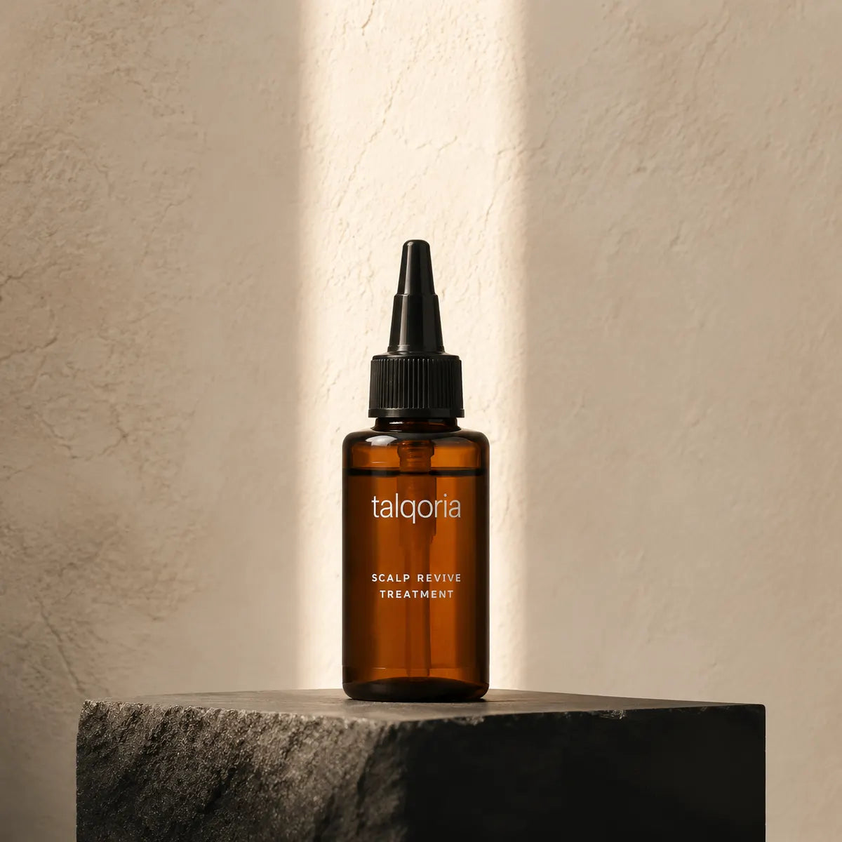 A small amber glass dropper bottle labeled talqoria Scalp Revive Treatment stands on a dark stone pedestal against a textured beige wall with warm sunlight and shadow streaks.