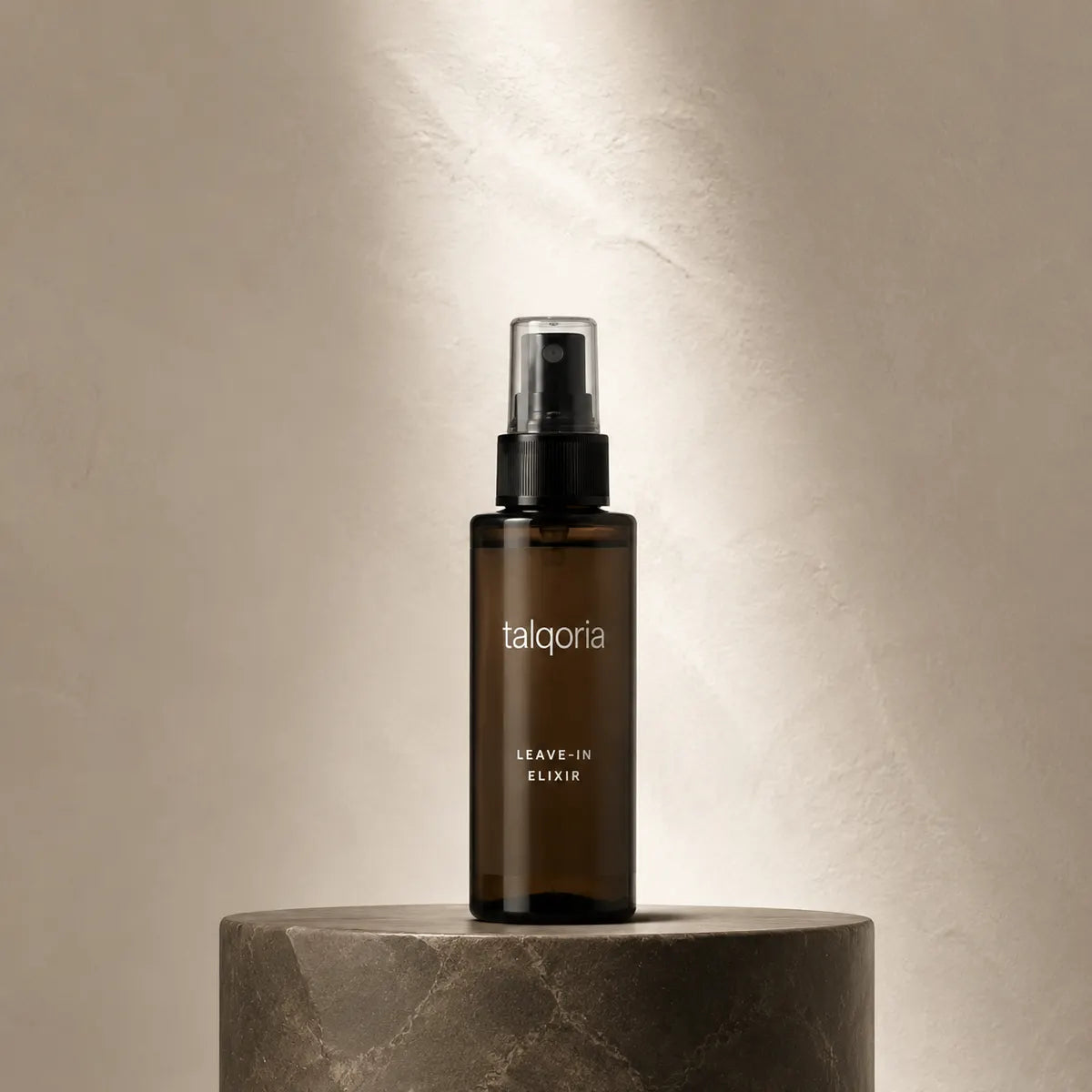 A dark amber glass spray bottle labeled 'talqoria LEAVE-IN ELIXIR' stands centered on a round stone pedestal against a softly lit beige wall.
